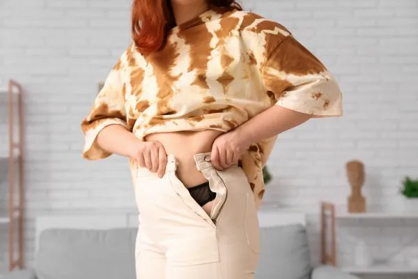 Image of woman trying to do her trousers up after pregnancy weight gain Maryhill